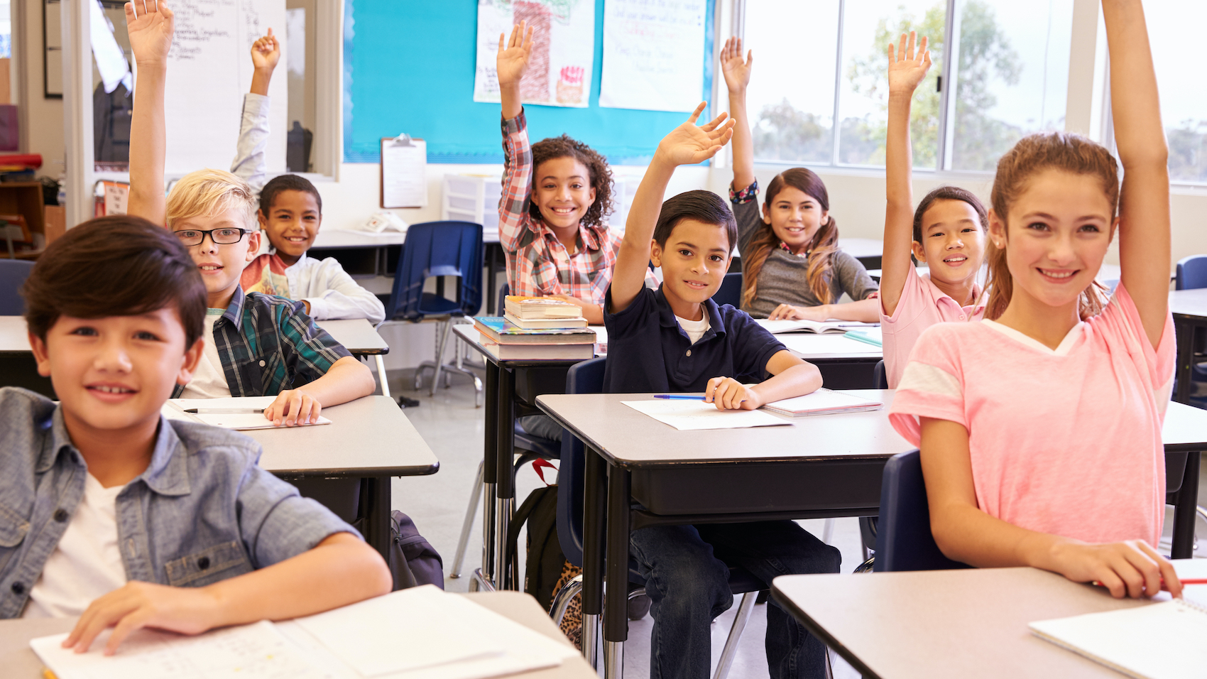 Elementary school kids in a classroom raising their hands.