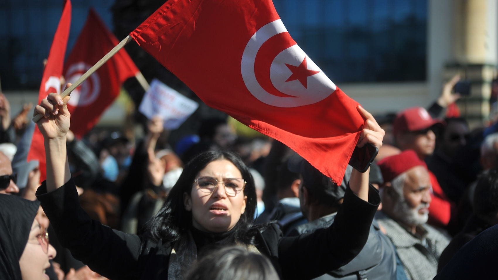 A woman raises the Tunisian flag during an Ennahda Party-led protest against the Tunisian president in Tunis, Tunisia on February 13, 2022. Photo: Mohamed Soufi.