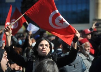 A woman raises the Tunisian flag during an Ennahda Party-led protest against the Tunisian president in Tunis, Tunisia on February 13, 2022. Photo: Mohamed Soufi.