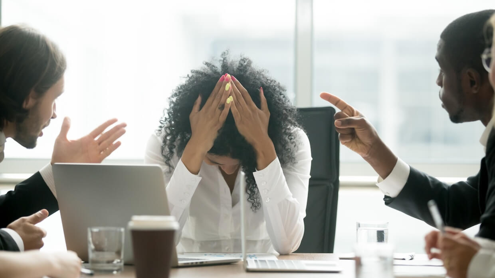 A distressed Black woman professional faces gender discrimination and workplace bullying, as male colleagues point fingers and place blame. The image highlights the emotional toll of inequality and harassment in professional environments. Photo: Dreamstime.