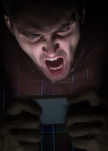 A man sits in the dark, staring angrily at his mobile phone. Photo: Raman Mistsechka.