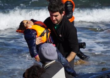 Refugee children are helped ashore after arriving by boat from Turkey on the Greek island of Lesbos, capturing a moment where relief and suffering coexist. Photo: Aleksandr Lutsenko.