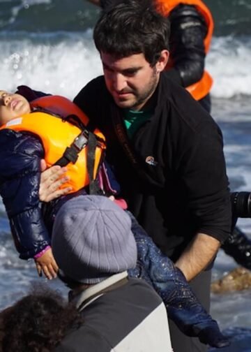 Refugee children are helped ashore after arriving by boat from Turkey on the Greek island of Lesbos, capturing a moment where relief and suffering coexist. Photo: Aleksandr Lutsenko.
