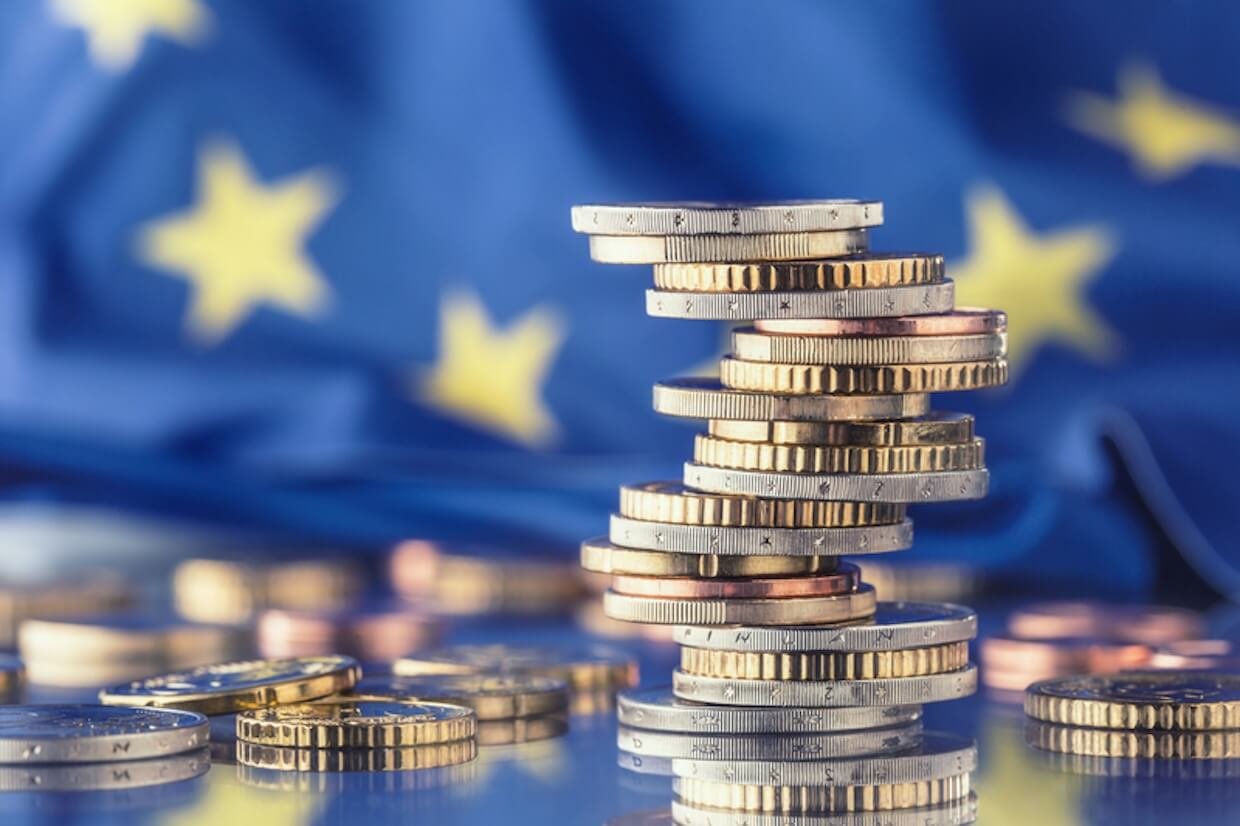 Stacks of euro coins placed before the flag of the European Union.